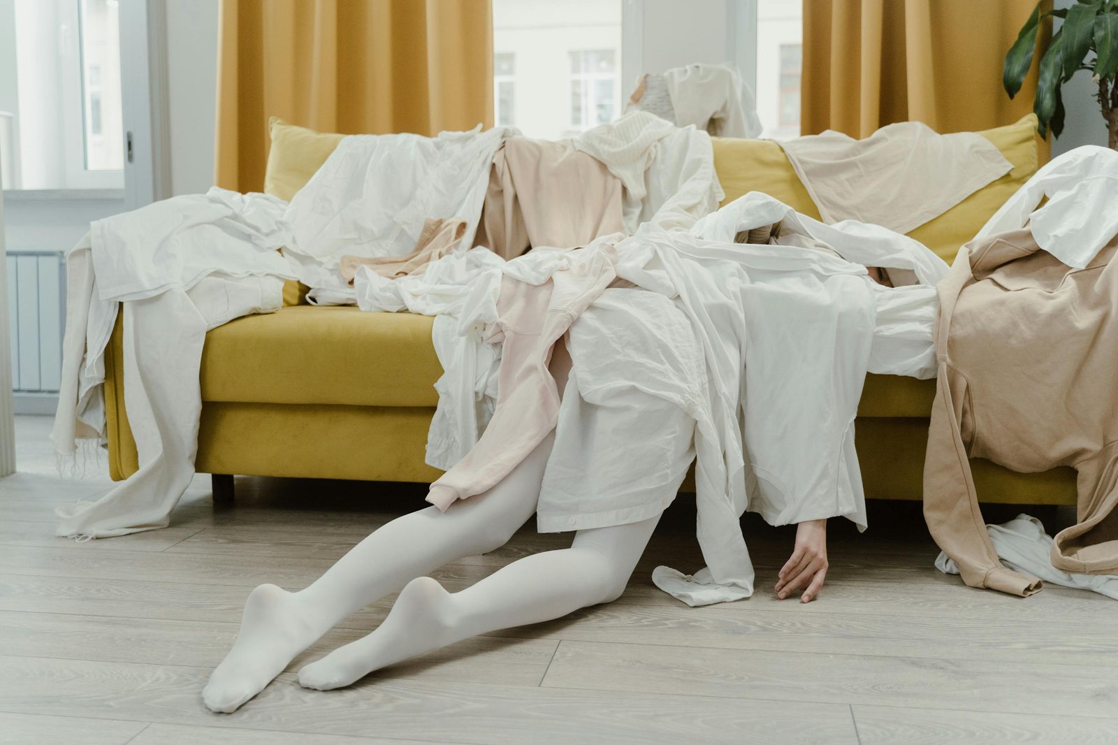 Complete disaster Artistic portrayal of a person buried under clothes on a couch, symbolizing chaos and disorder.