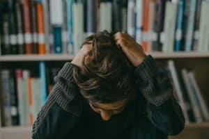 Women's Mental load A child appears stressed and frustrated while seated in a library, holding their head.